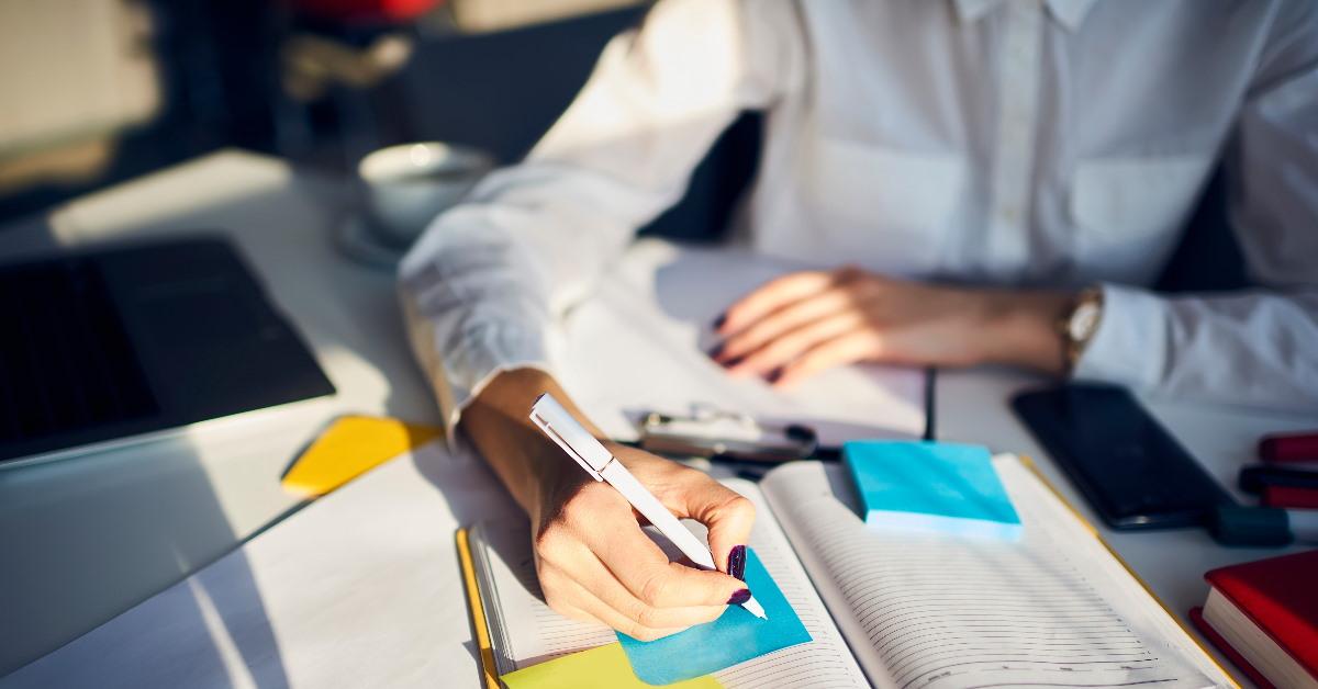 woman writing on sticky notes inside book using pen