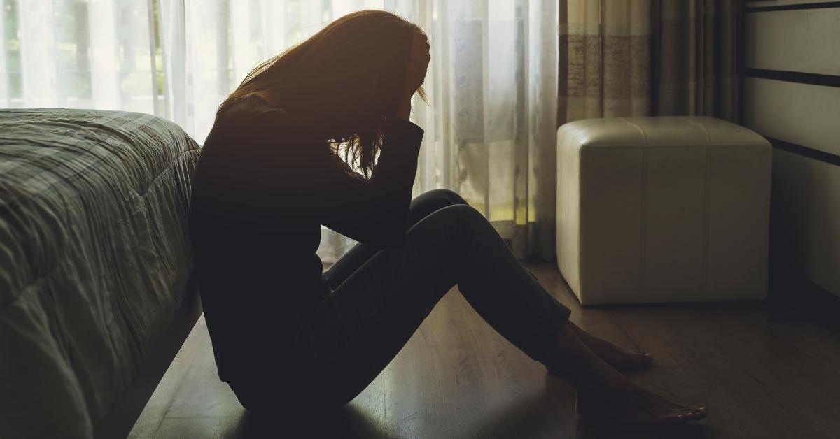 depressed woman sitting with head in hands in the dark bedroom