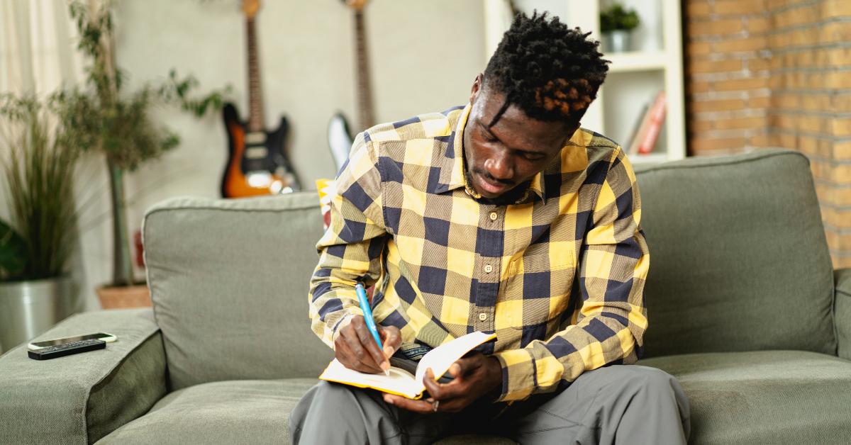 man writing down notes while sitting on sofa