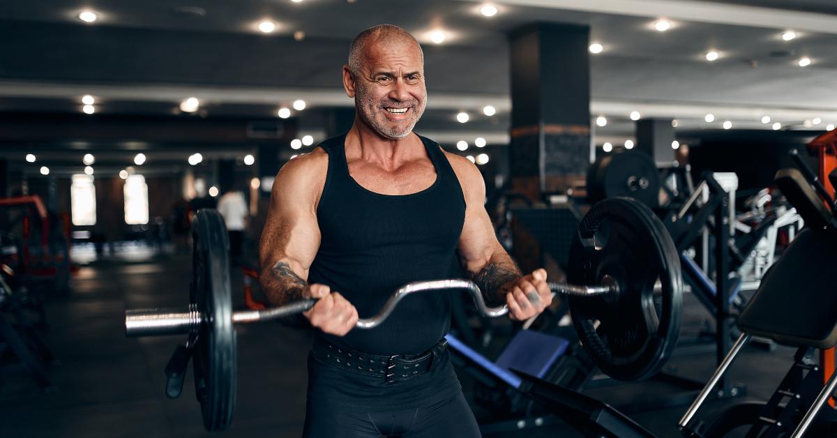 older man working out in gym doing exercises with barbell