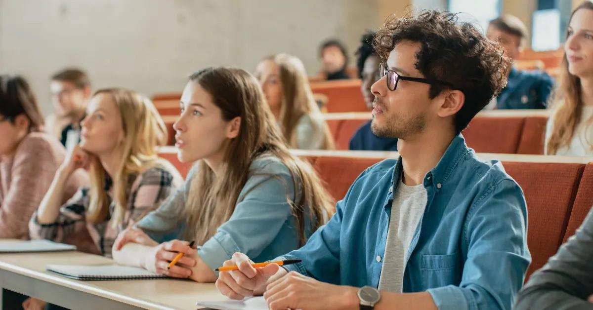 multi ethnic students listening to a lecturer and writing in notebooks