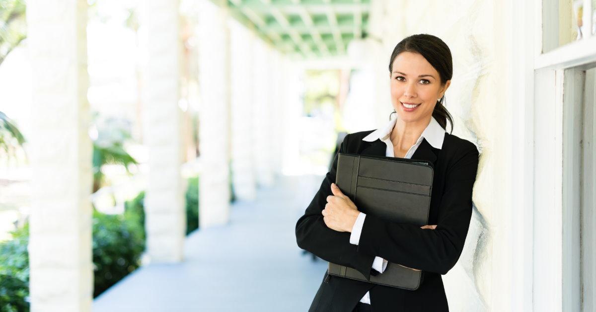 attractive female real estate agent in suit standing in corridor holding files in hand