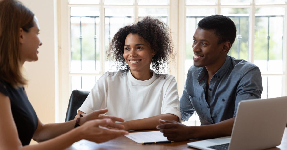 african american couple sitting at table talking to female real estate agent 