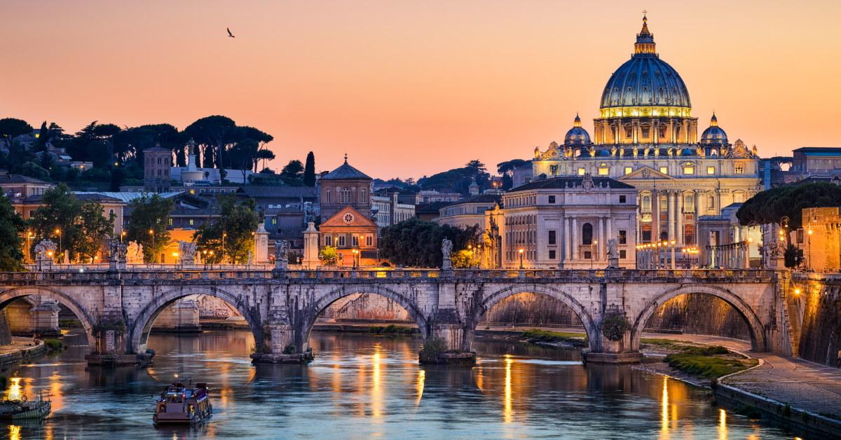 night time view of basilica st peter in front of water with buildings having golden lights