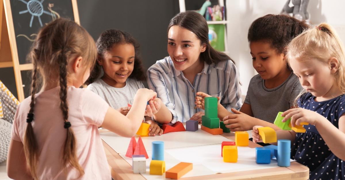 children and nursery teacher playing with building blocks