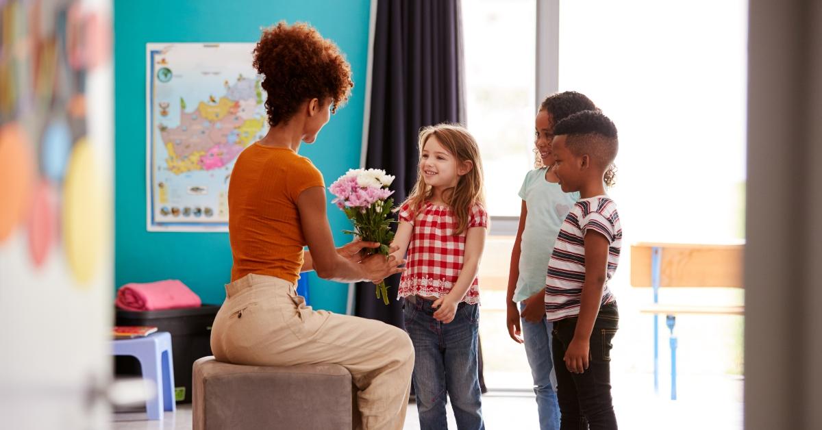 elementary school pupils giving female teacher gift of flowers