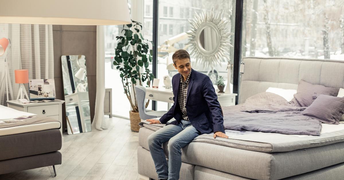 man resting on new bed in furniture store