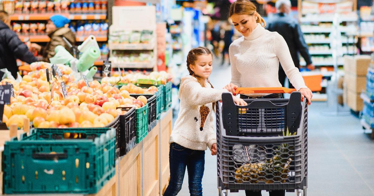 mother and daughter shopping for grocery using shopping trolley at supermarket