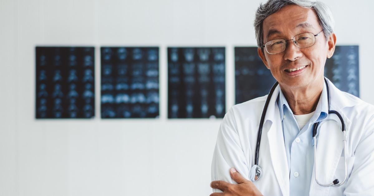 senior asian male doctor wearing overalls and stethoscope standing in front of radiology reports