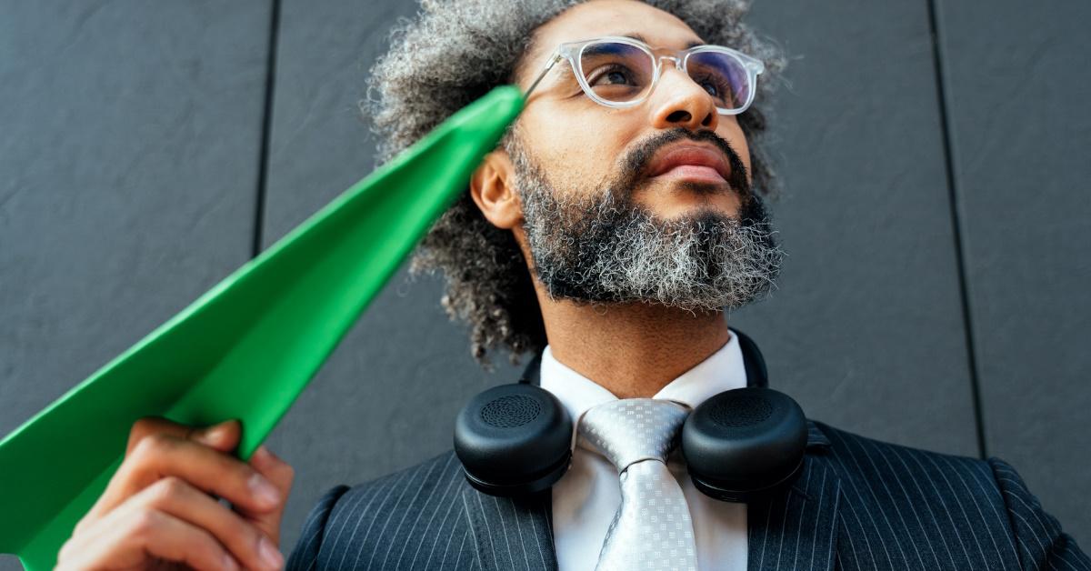 man dressed in a suit, holding a green paper plane