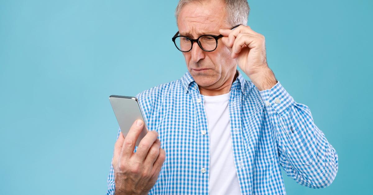 Mature man squinting using mobile phone