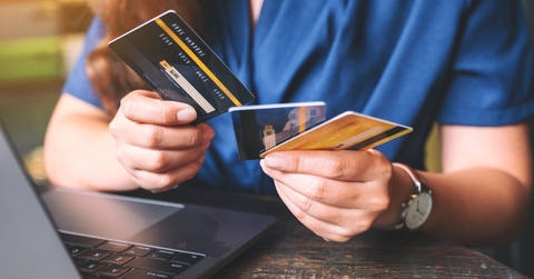 woman holding and choosing credit cards while using laptop