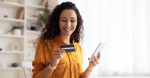 Smiling woman looking at credit card and holding phone