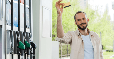 man holds credit card by gas pumps