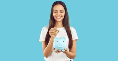 A happy woman is holding a piggy bank and about to insert a coin.