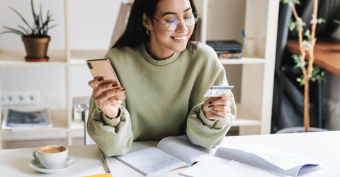A woman smiles as she holds her phone and a credit card. 