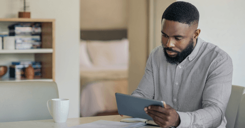 A man is looking at his tablet at the kitchen counter. 