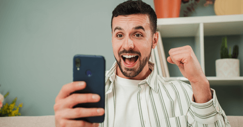 A man cheers while playing a game on his phone.