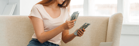 A woman counts a stack of cash on her couch.