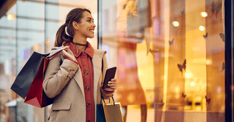 A woman shopper holds shopping bags and passes by a storefront. 
