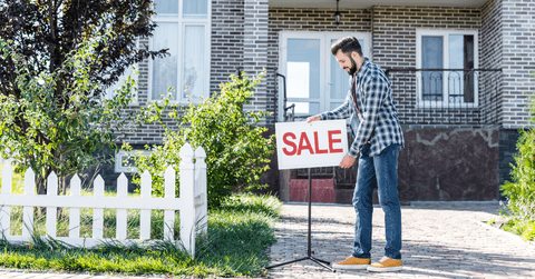 Man putting for sale sign in front of house