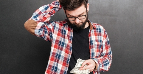 confused man standing over chalkboard while holding money