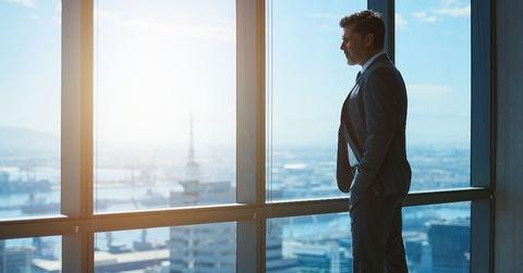 mature businessman looking through large windows at city below