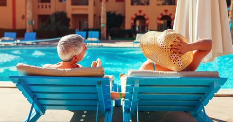 senior couple relaxing by swimming pool lying on chaise-longues