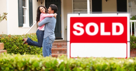 hispanic couple outside home with sold sign