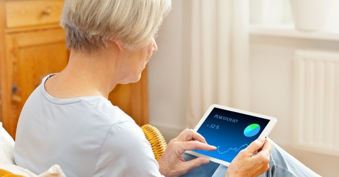 senior woman in her living room checking her investment portfolio on a tablet