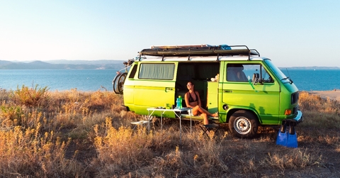 Young attractive female sitting in old timer camper van on a hill 