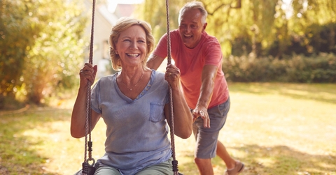 retired couple having fun with man pushing woman on garden swing