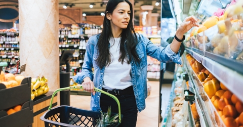 young woman holding grocery basket in a store while picking grocery