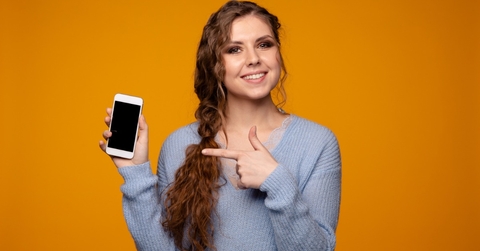 smiling young woman wearing grey sweatshirt holding smartphone