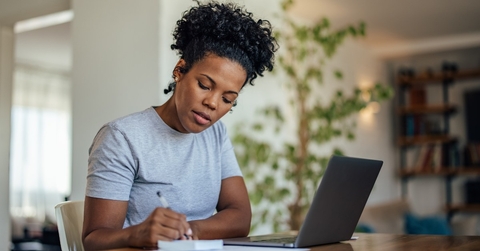african american woman writing on notepad in front of laptop