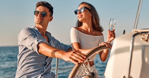 happy couple wearing shades while holding glass of champagne partying on yacht