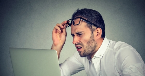 man with glasses squinting eyes at laptop 