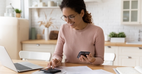 female works with financial papers at home counting on calculator