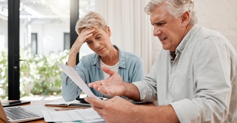 senior couple sitting at table with papers stressing at documents in hands