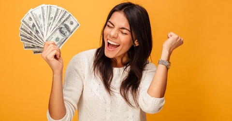 woman wearing white sweater screaming in excitement while holding money in hand in front of orange background