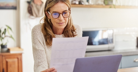 woman sitting at counter top in kitchen reviewing documents while using computer at home