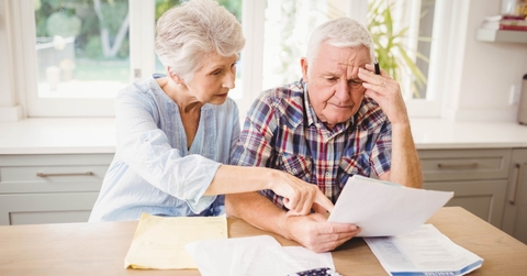 senior couple sitting at table reviewing taxes while doing calculations 