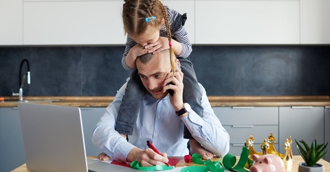 daughter sitting on her dads shoulders while he's working on his laptop