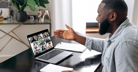 happy african american man sitting on work desk at office using laptop to have virtual video conference with colleagues