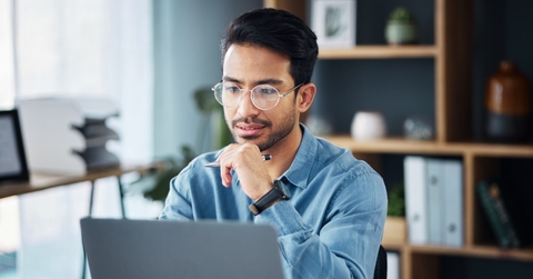 young asian businessman sitting at work desk using laptop for work besides coffee cup