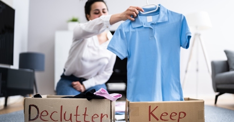 Woman sorting wardrobe into brown boxes with "declutter" and "keep" labels.