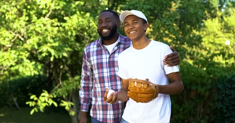 happy father praising son playing baseball in park