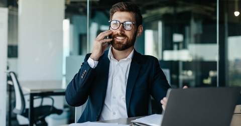 young handsome businessman talking on phone sitting at table with laptop and papers in office