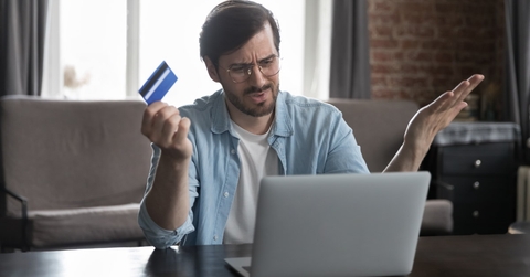 man annoyed at laptop while holding card in hand 