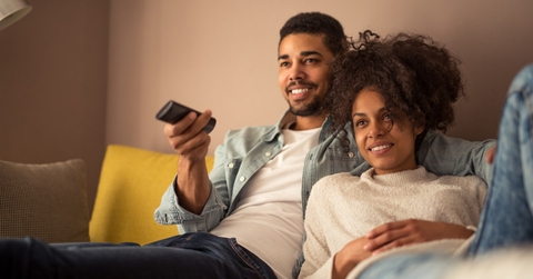 african american couple sitting on couch at home using remote while watching tv